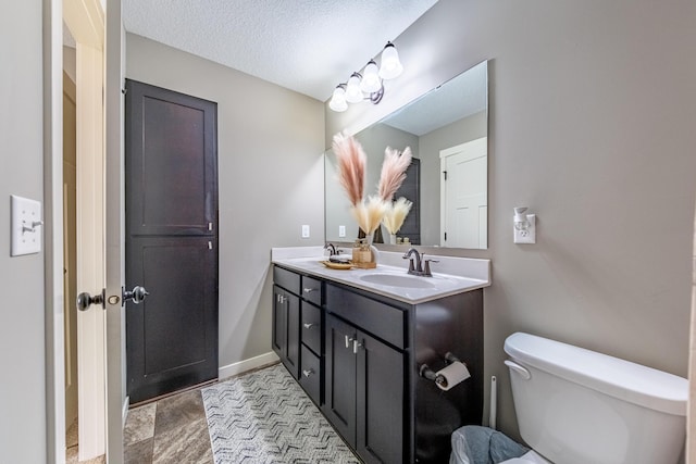 full bathroom featuring a sink, a textured ceiling, toilet, and double vanity