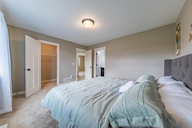 bedroom with baseboards, visible vents, light colored carpet, a walk in closet, and a closet