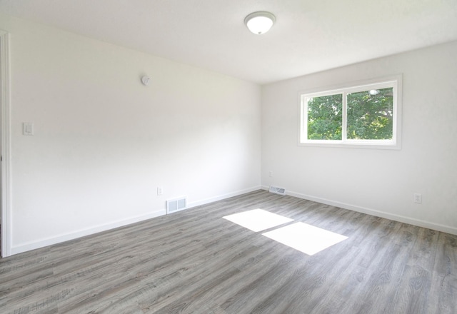 empty room featuring wood finished floors, visible vents, and baseboards