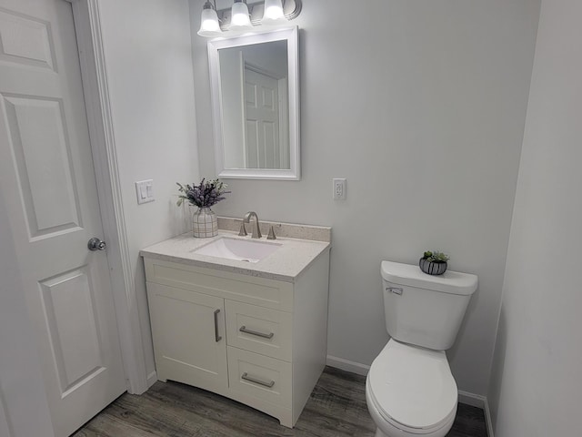 bathroom featuring toilet, baseboards, wood finished floors, and vanity