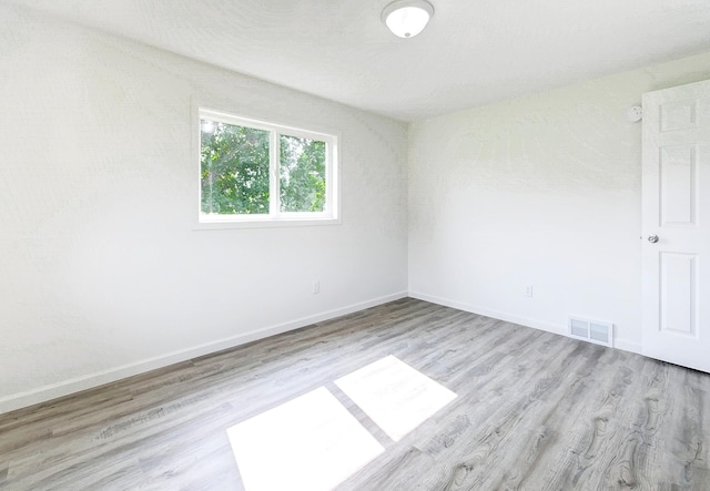 empty room with light wood-style floors, visible vents, and baseboards