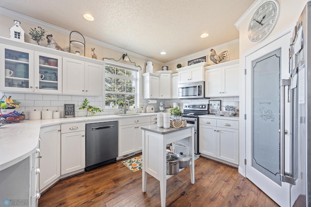 kitchen featuring crown molding, dark wood finished floors, white cabinets, stainless steel appliances, and a sink