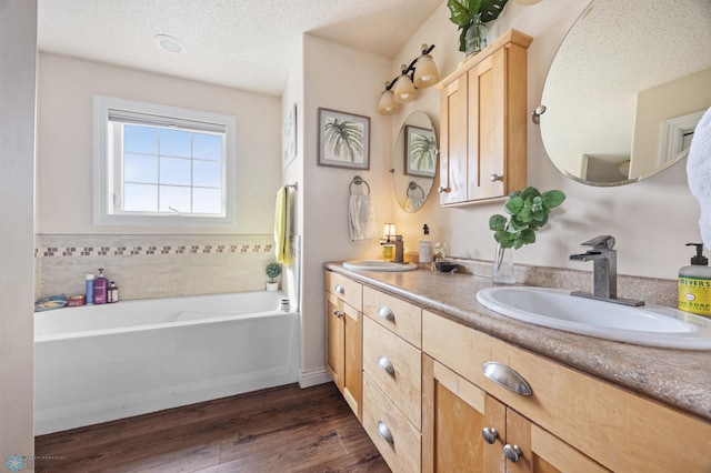 full bathroom featuring a textured ceiling, double vanity, wood finished floors, and a sink