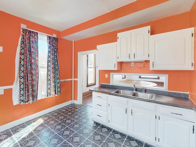 kitchen featuring a textured ceiling, a sink, white cabinetry, baseboards, and dark countertops