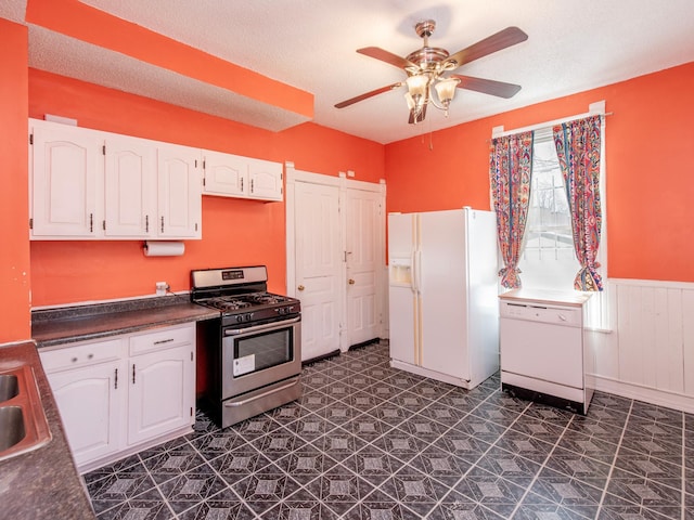 kitchen with a wainscoted wall, white appliances, a sink, white cabinets, and dark countertops