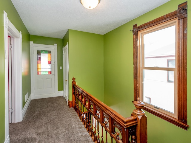 corridor featuring carpet, baseboards, a textured ceiling, and an upstairs landing