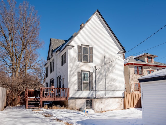 snow covered property featuring a deck, a chimney, and fence