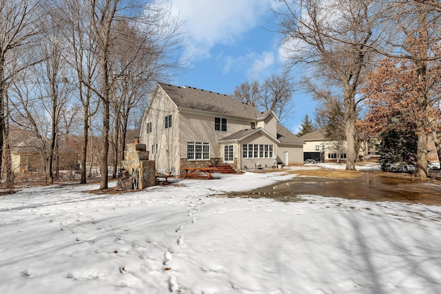 snow covered rear of property featuring stone siding