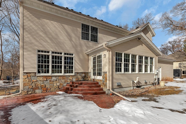 snow covered rear of property with stone siding