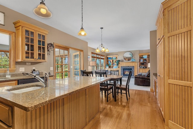 kitchen featuring a sink, open floor plan, hanging light fixtures, light wood-type flooring, and glass insert cabinets