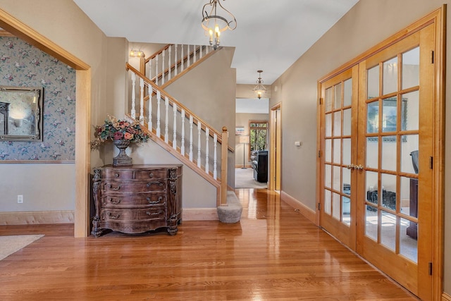 entrance foyer with baseboards, stairs, french doors, light wood-style floors, and a chandelier