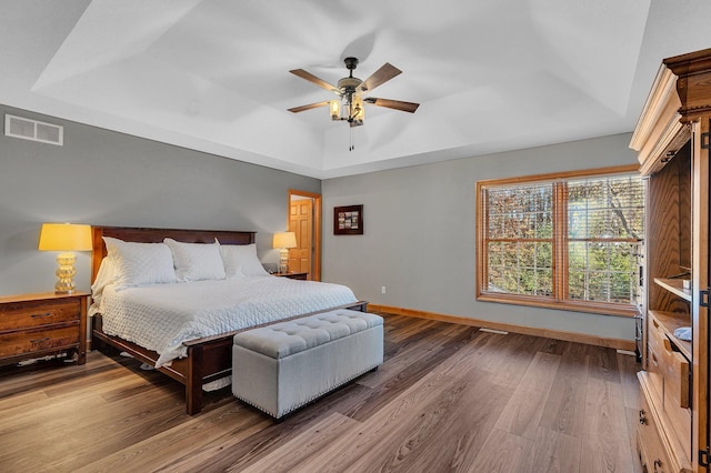 bedroom with baseboards, visible vents, ceiling fan, wood finished floors, and a tray ceiling