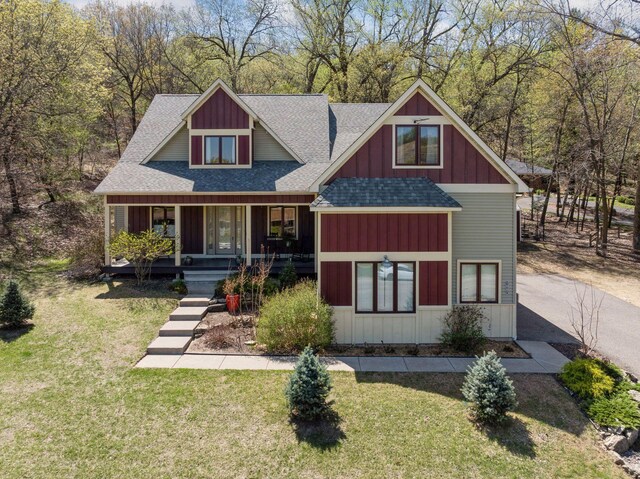 view of front of home featuring roof with shingles, a front yard, covered porch, and board and batten siding
