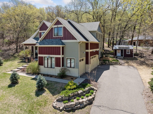 view of front of house featuring board and batten siding, asphalt driveway, a shingled roof, and a front yard