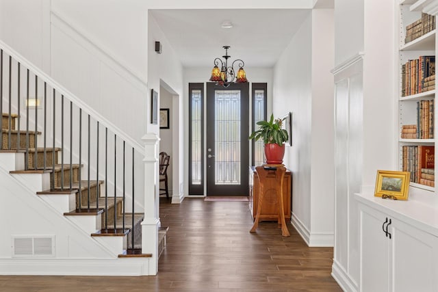 foyer entrance with dark wood finished floors, a chandelier, stairway, and a decorative wall
