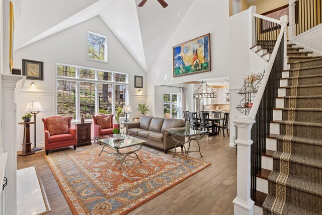 living room with a ceiling fan, high vaulted ceiling, stairs, plenty of natural light, and wood finished floors