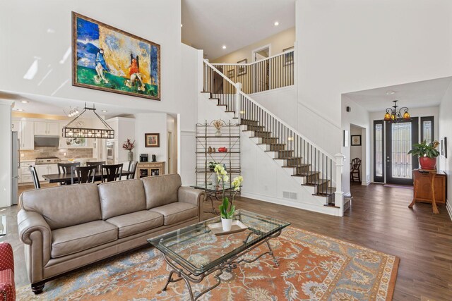 living room featuring stairway, a chandelier, a towering ceiling, wood finished floors, and baseboards