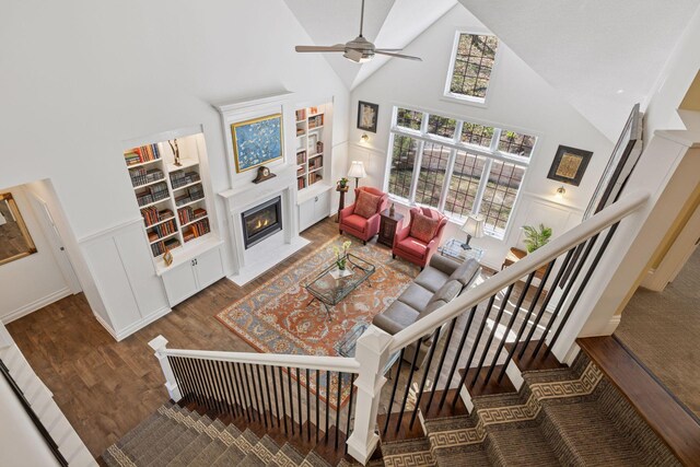 living room with high vaulted ceiling, a fireplace with flush hearth, wood finished floors, ceiling fan, and stairs