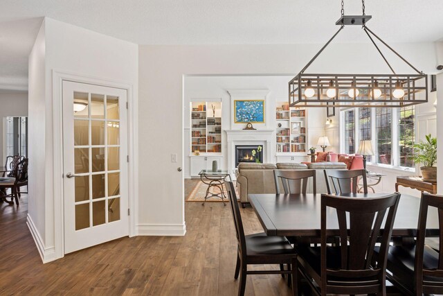 dining space featuring dark wood-style floors, a warm lit fireplace, baseboards, and a chandelier