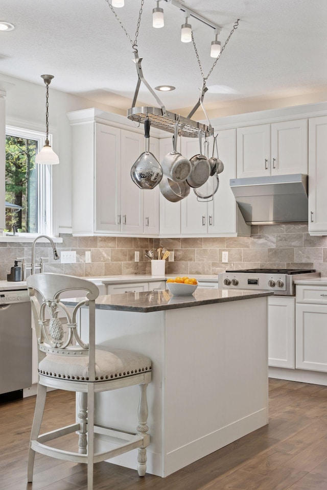 kitchen featuring wall chimney exhaust hood, stainless steel appliances, white cabinets, light wood-type flooring, and tasteful backsplash