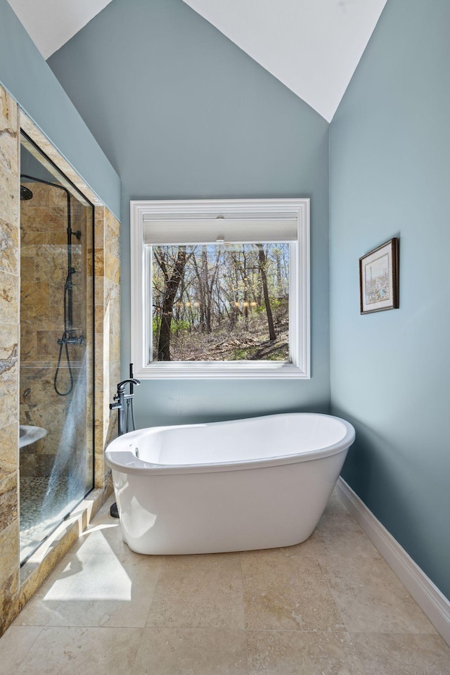bathroom with a stall shower, a freestanding bath, vaulted ceiling, and baseboards