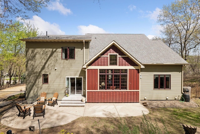 back of property with a patio area, a shingled roof, board and batten siding, and a fire pit