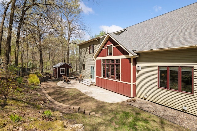 back of house featuring a patio, a shed, an outdoor structure, and roof with shingles