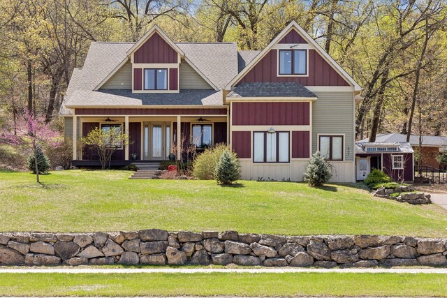 craftsman-style home with ceiling fan, a shingled roof, covered porch, and a front lawn