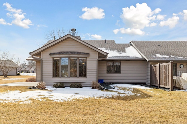 snow covered back of property featuring a lawn and a shingled roof