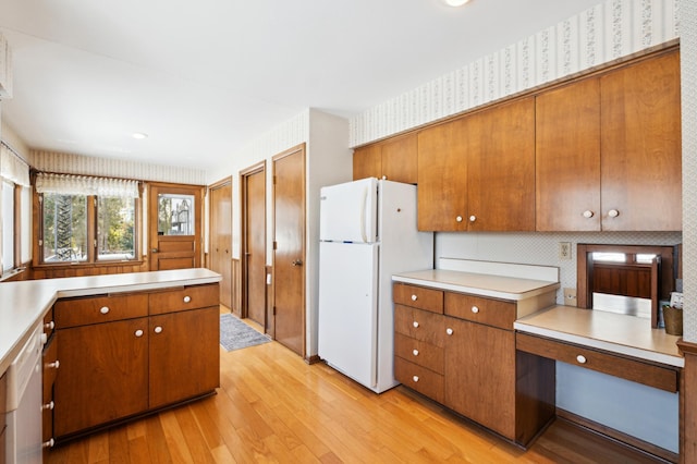 kitchen featuring light countertops, brown cabinetry, freestanding refrigerator, light wood-type flooring, and wallpapered walls