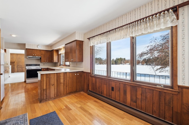 kitchen with electric stove, a wainscoted wall, a baseboard heating unit, under cabinet range hood, and wallpapered walls