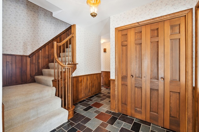 interior space with stairway, stone finish flooring, wainscoting, wood walls, and wallpapered walls