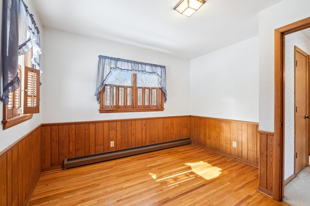 empty room with a healthy amount of sunlight, a baseboard heating unit, and wainscoting