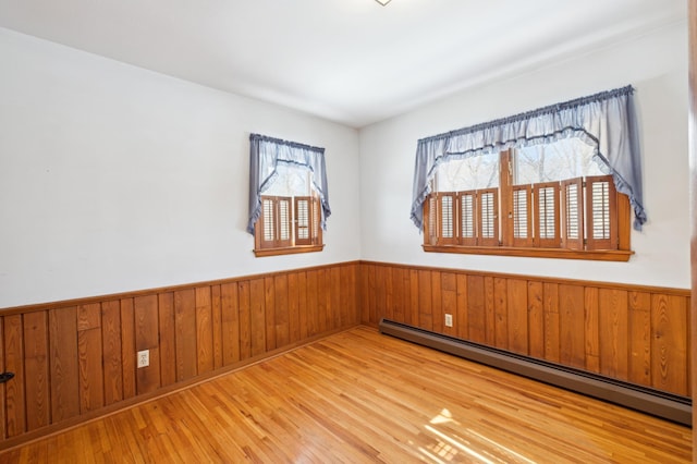 empty room with wooden walls, a baseboard heating unit, wood finished floors, and wainscoting