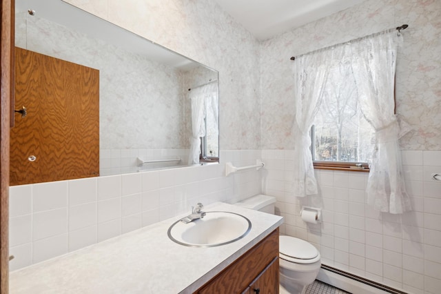 bathroom featuring wallpapered walls, wainscoting, toilet, baseboard heating, and tile walls