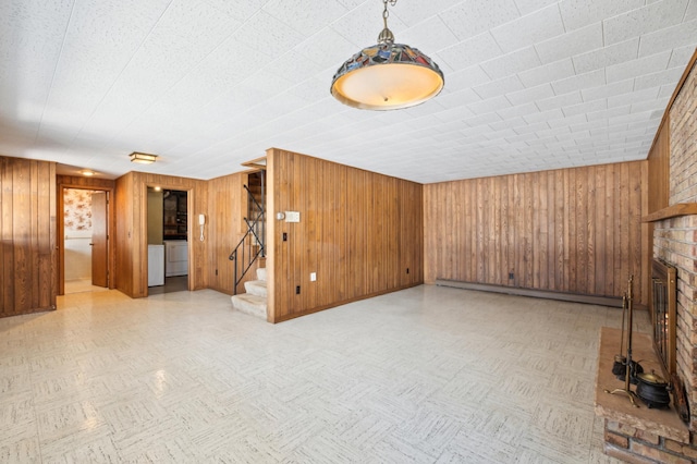 unfurnished living room featuring stairs, baseboard heating, a brick fireplace, wood walls, and tile patterned floors