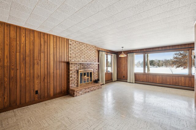 unfurnished living room with wooden walls, a baseboard heating unit, baseboards, a brick fireplace, and tile patterned floors