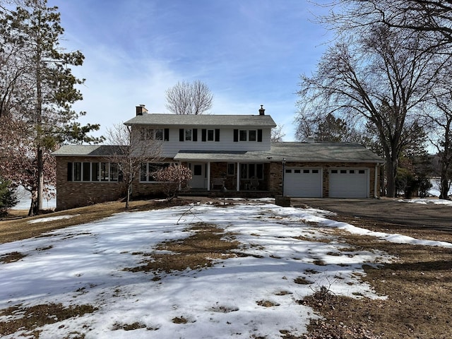 traditional-style home with aphalt driveway, brick siding, a garage, and a chimney