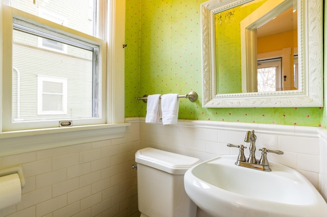 half bath featuring a sink, wallpapered walls, toilet, and a wainscoted wall