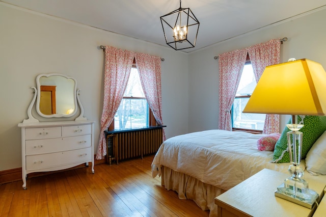 bedroom with radiator heating unit, wood finished floors, and a notable chandelier