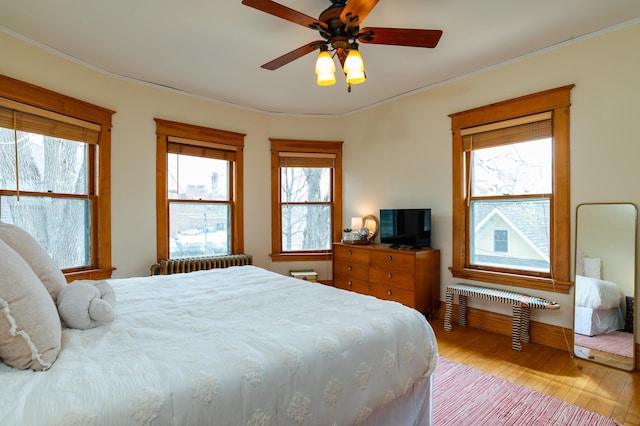 bedroom featuring ceiling fan, ornamental molding, radiator heating unit, and light wood-style floors