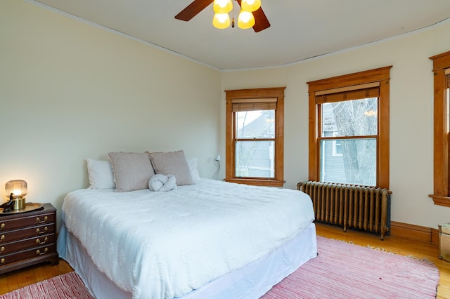 bedroom with light wood-type flooring, crown molding, radiator heating unit, and ceiling fan