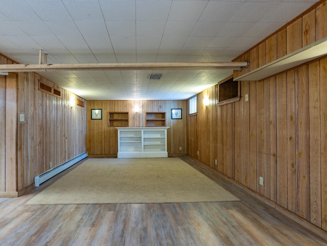 basement with a baseboard heating unit, visible vents, light wood-style floors, and wooden walls