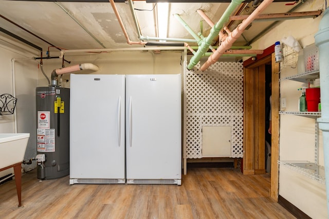 unfinished basement featuring a sink, gas water heater, wood finished floors, and freestanding refrigerator