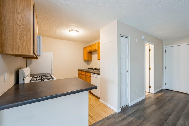 kitchen with white appliances, a textured ceiling, dark countertops, a sink, and wood finished floors