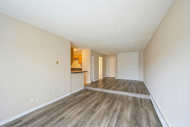 unfurnished living room featuring a baseboard heating unit, baseboards, and wood finished floors