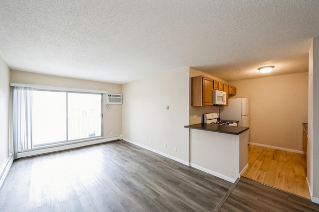 unfurnished living room featuring dark wood-type flooring, a textured ceiling, baseboard heating, an AC wall unit, and baseboards