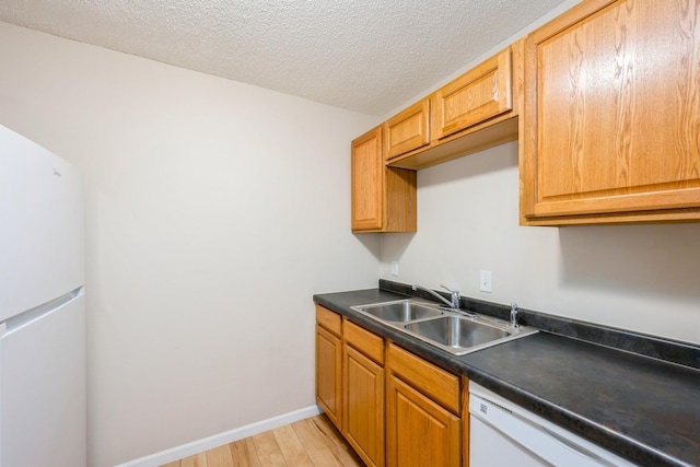 kitchen featuring a sink, light wood-type flooring, white appliances, dark countertops, and a textured ceiling