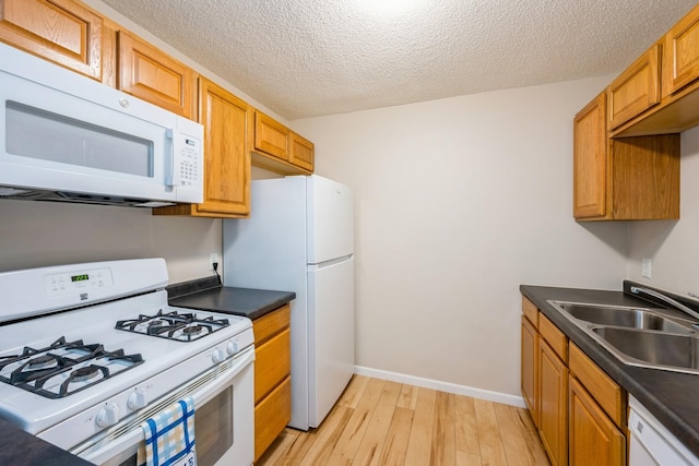 kitchen featuring light wood-style flooring, a sink, a textured ceiling, dark countertops, and white appliances