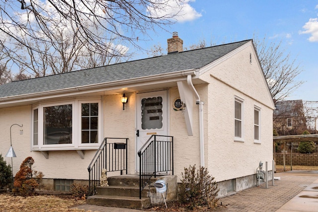 view of front facade with a shingled roof, stucco siding, and a chimney